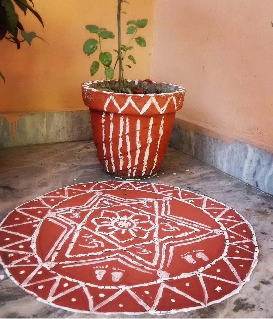 An Aipan circle in red geru and white rice paste on a courtyard floor, with Lakshmi's footprints drawn in