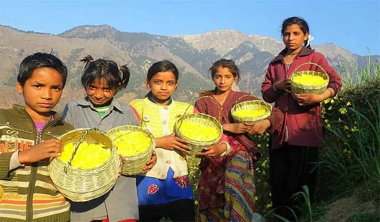 Children holding woven baskets full of yellow flowers, with the mountains behind them